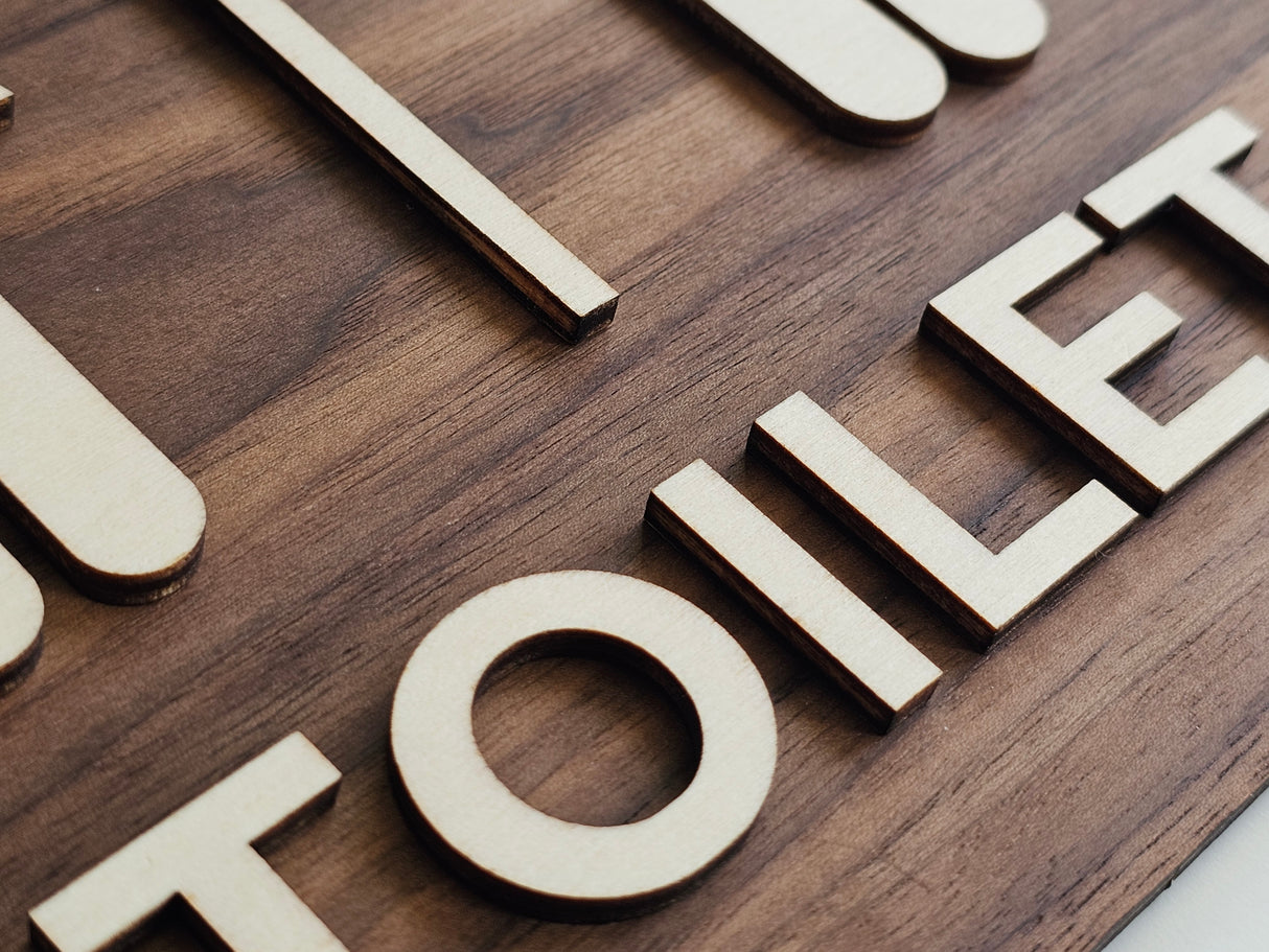 Nærbillede af toilet skilt i træ med lyse bogstaver på mørkt valnødstræ