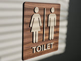 Toilet skilt i træ med tekst og piktogram set fra vinkel